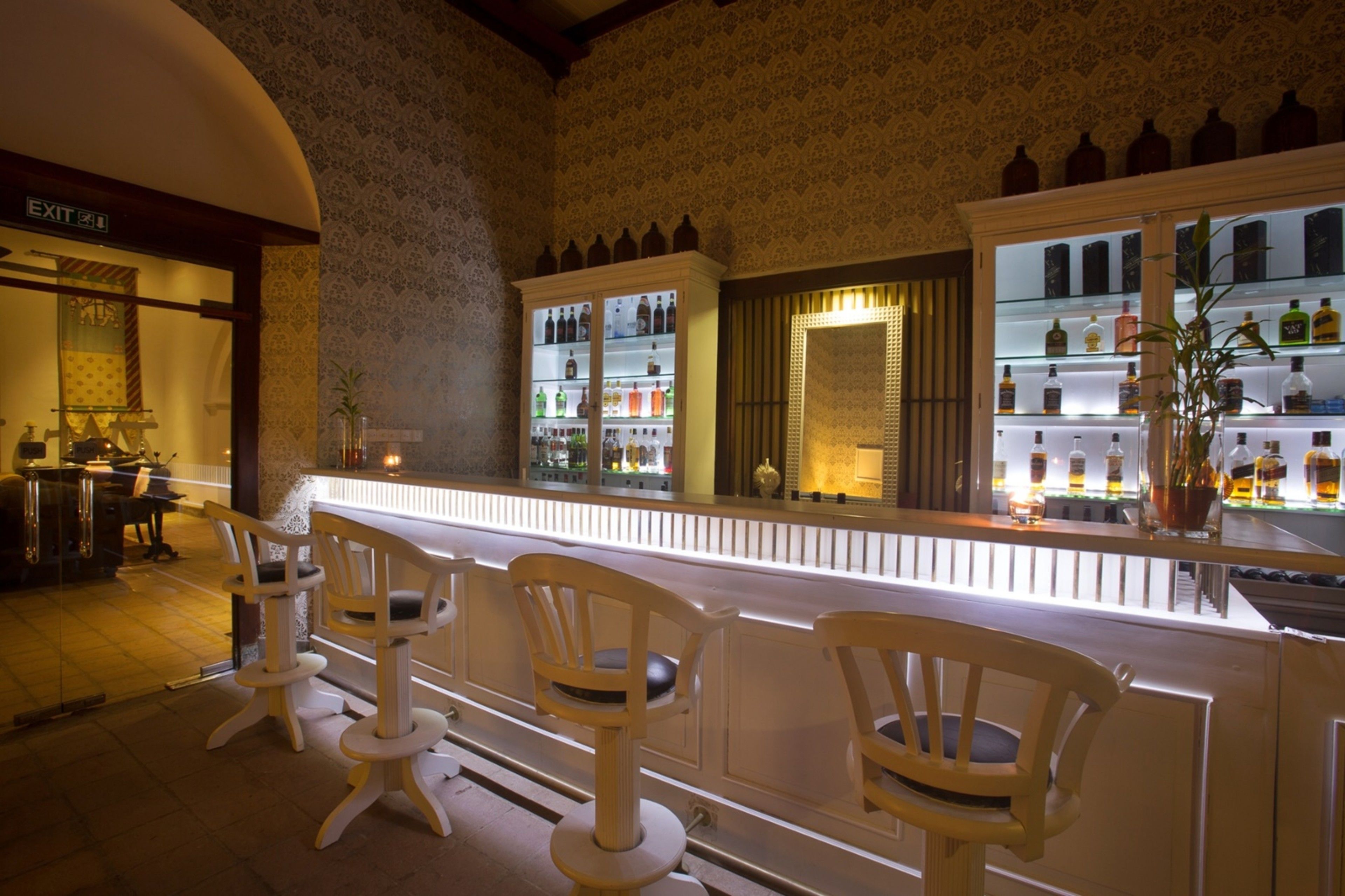 Zona de bar con una barra larga, taburetes acolchados y estantes llenos de botellas.