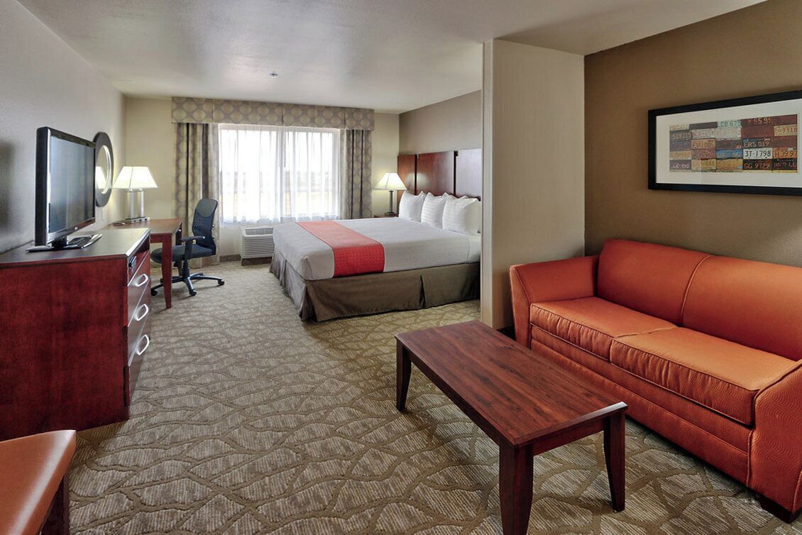 A hotel room with a bed, a sofa, a desk with a television, a chair, and a lamp.