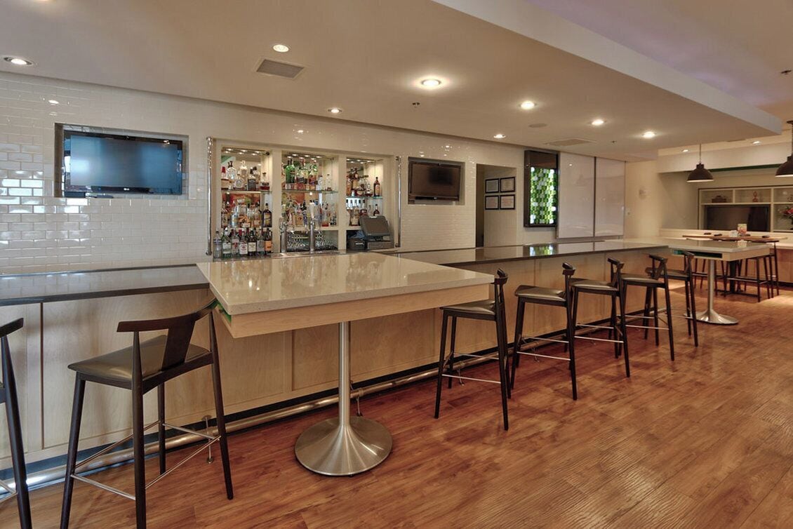 A bar area with a long counter, multiple stools, and a television mounted on the wall.
