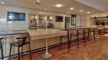 A bar area with a long counter, multiple stools, and a television mounted on the wall.