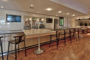 Una zona de bar con una barra larga, varios taburetes y un televisor montado en la pared.