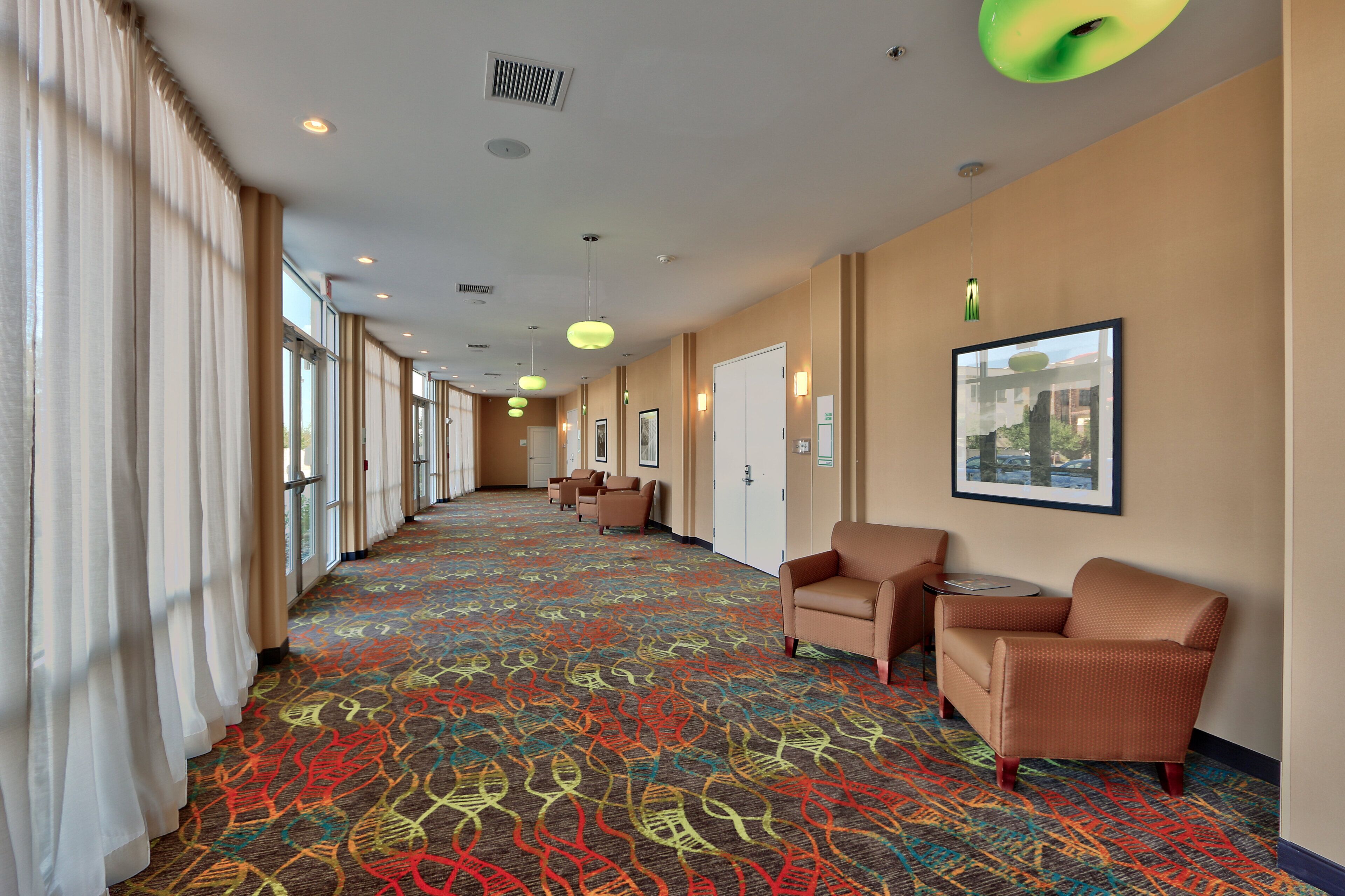 A hotel corridor with patterned carpet, seating areas, and framed artwork on the walls.