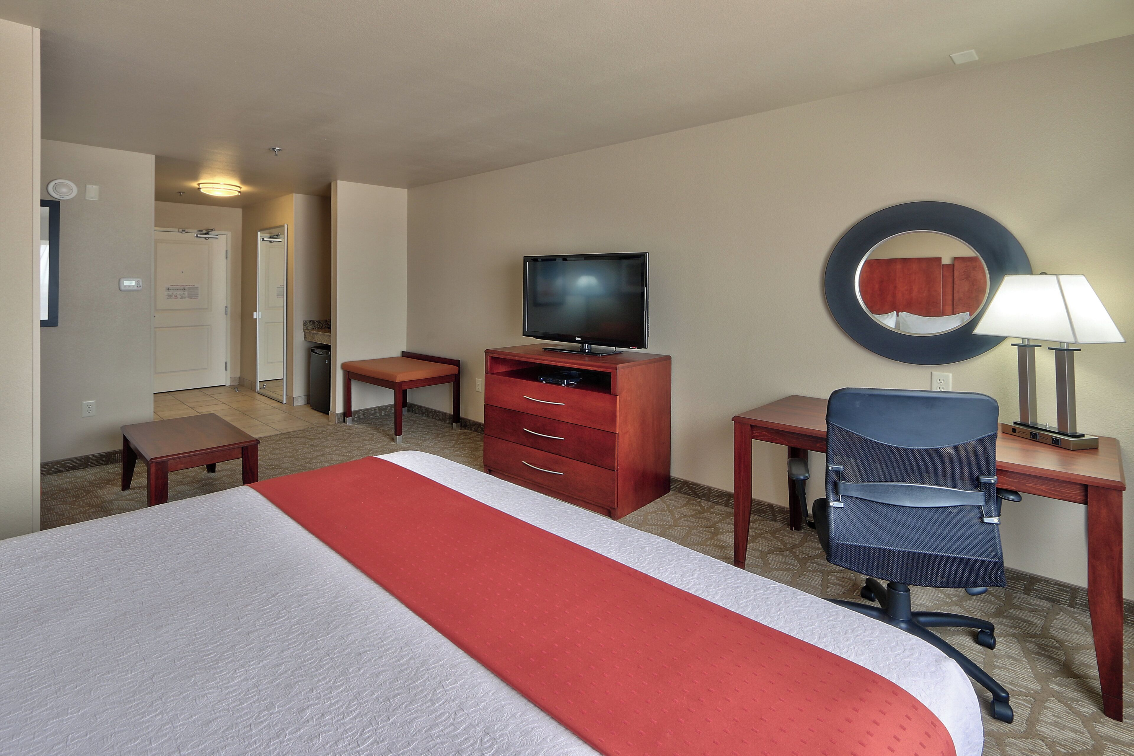 A hotel room with a bed, a desk, a chair, a television, and a mirror.
