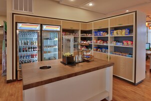 Una estación autoservicio de bebidas con dispensadores refrigerados y una máquina de café, rodeada de estantes llenos de refrigerios y productos envasados.