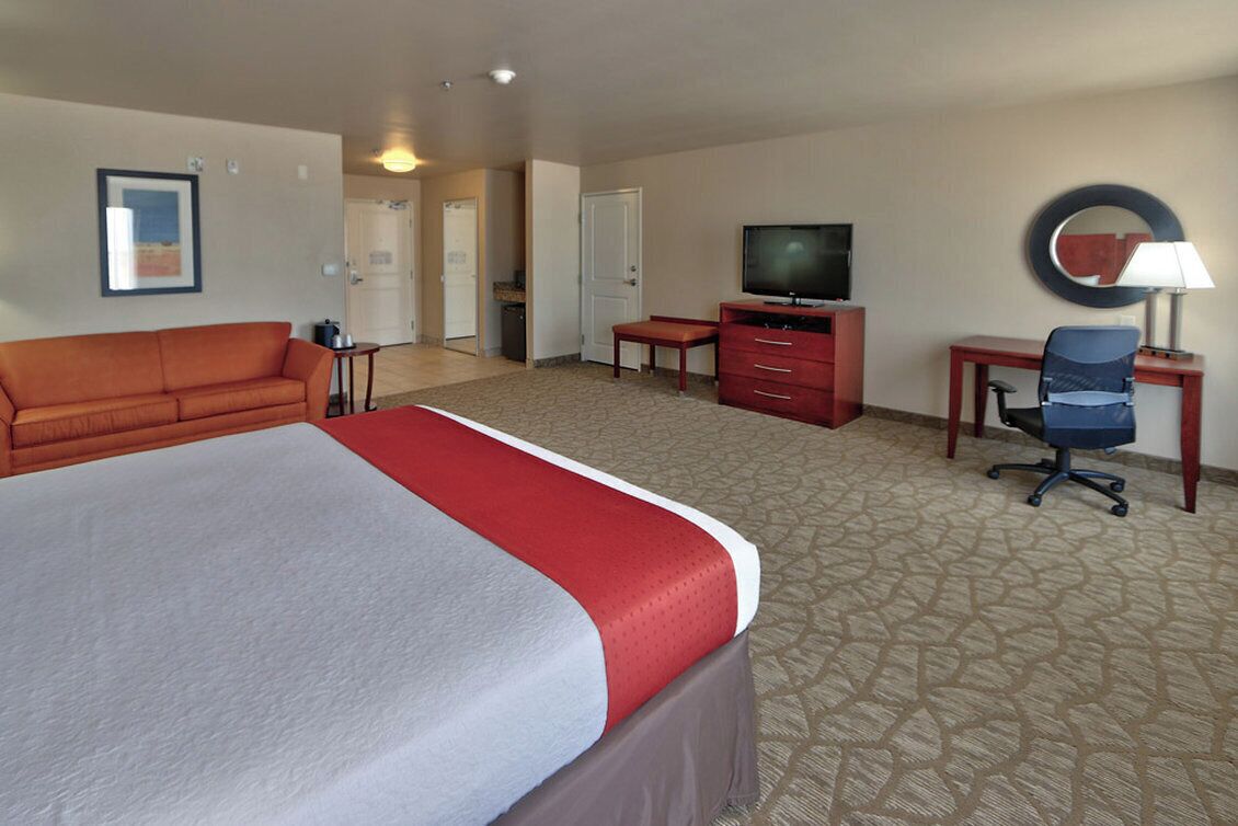 A hotel room with a large bed, a sofa, a TV, a desk, and a chair.