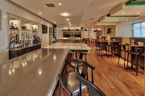 A bar area with a long counter, multiple seating options, and a television screen mounted on the wall.