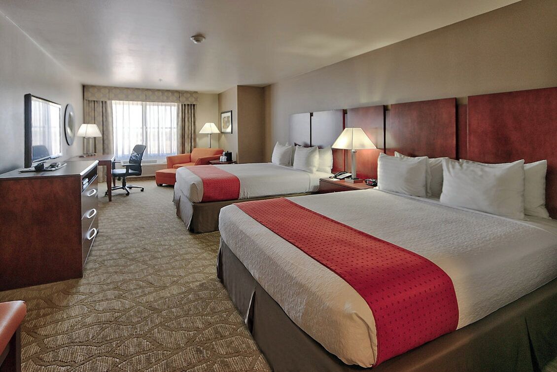 A hotel room with two beds, a desk with a chair, a television, and a window with curtains.