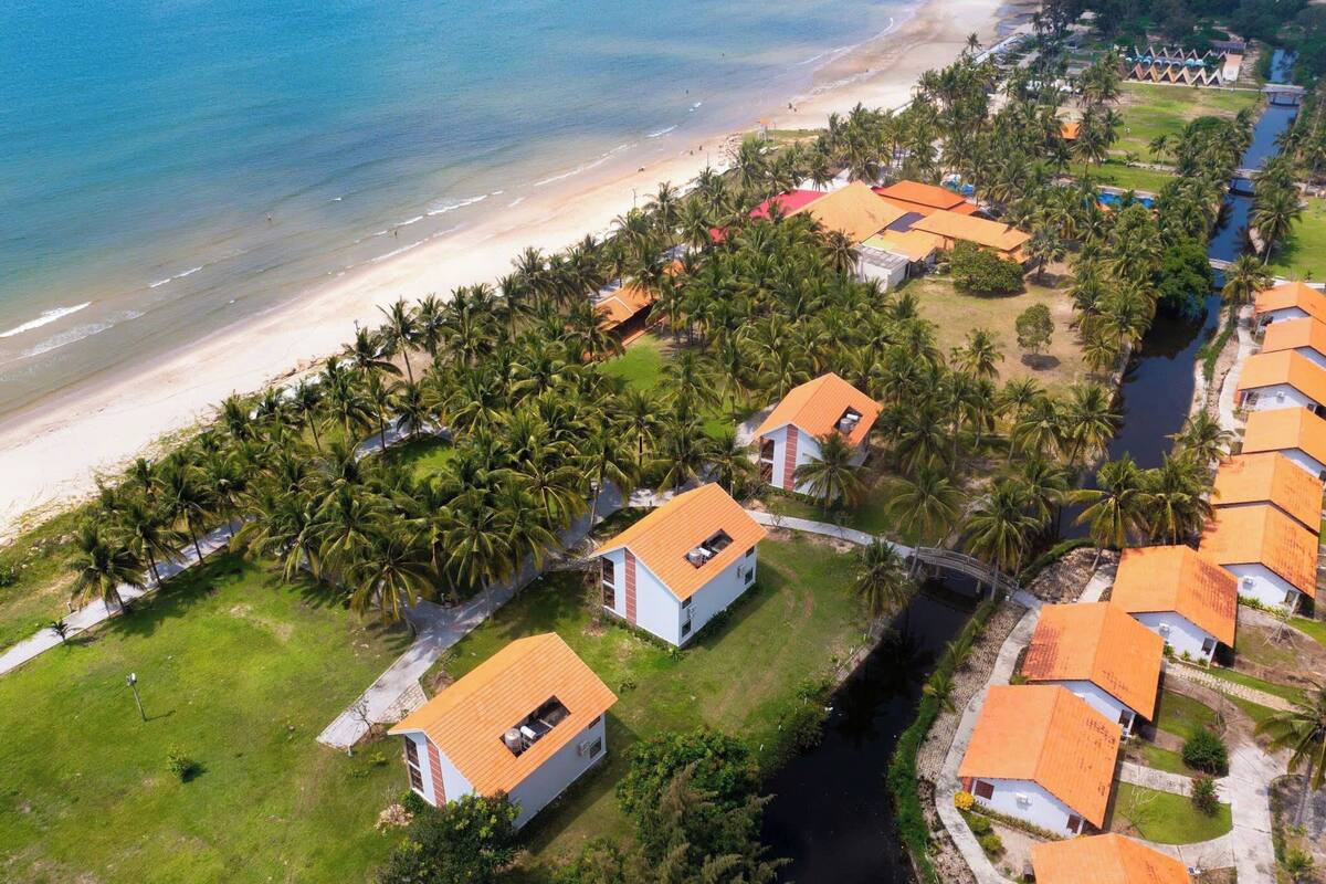 Ein Küstenresort mit Bungalow-Unterkünften, einem Strand und Palmen.