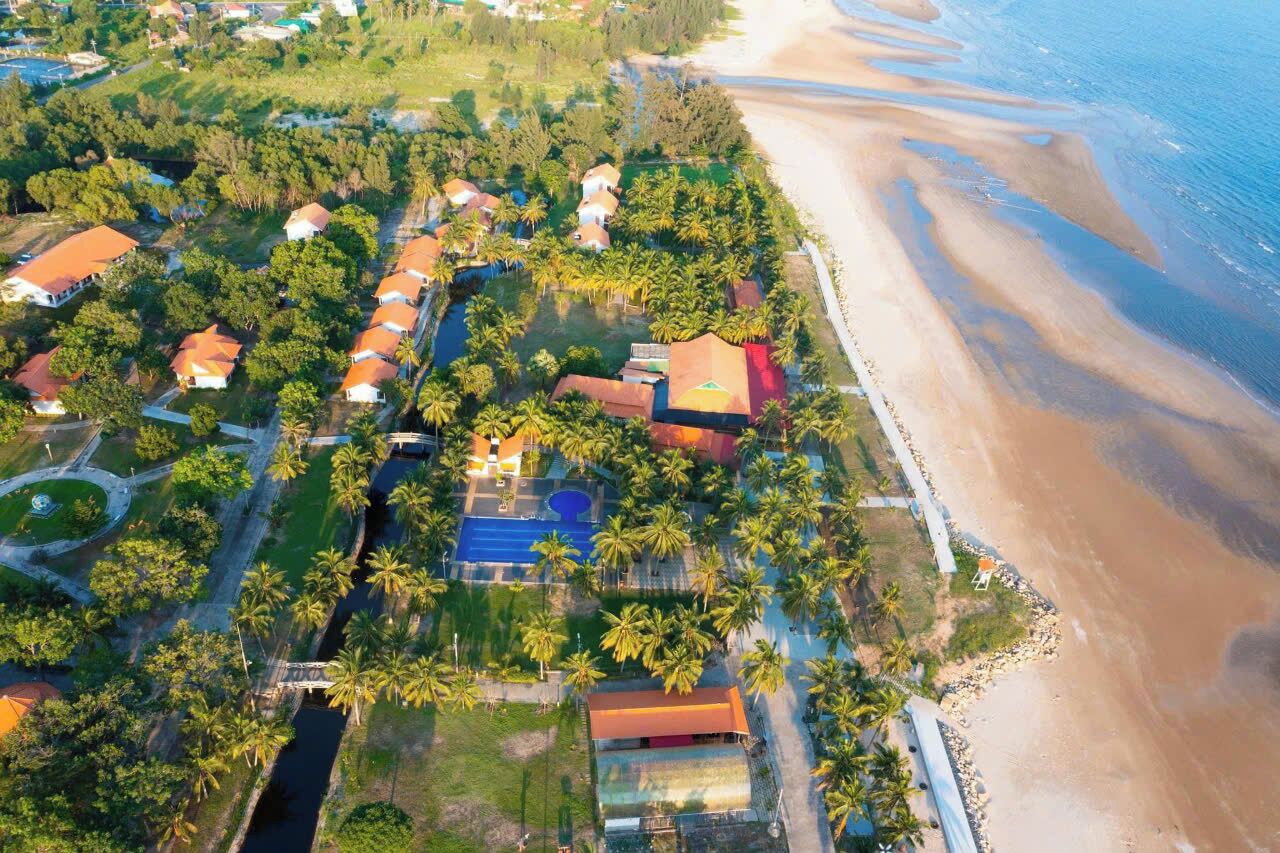 Vista aérea de un complejo turístico costero con varias edificaciones tipo bungaló, un área de piscina central y una playa adyacente a la propiedad.