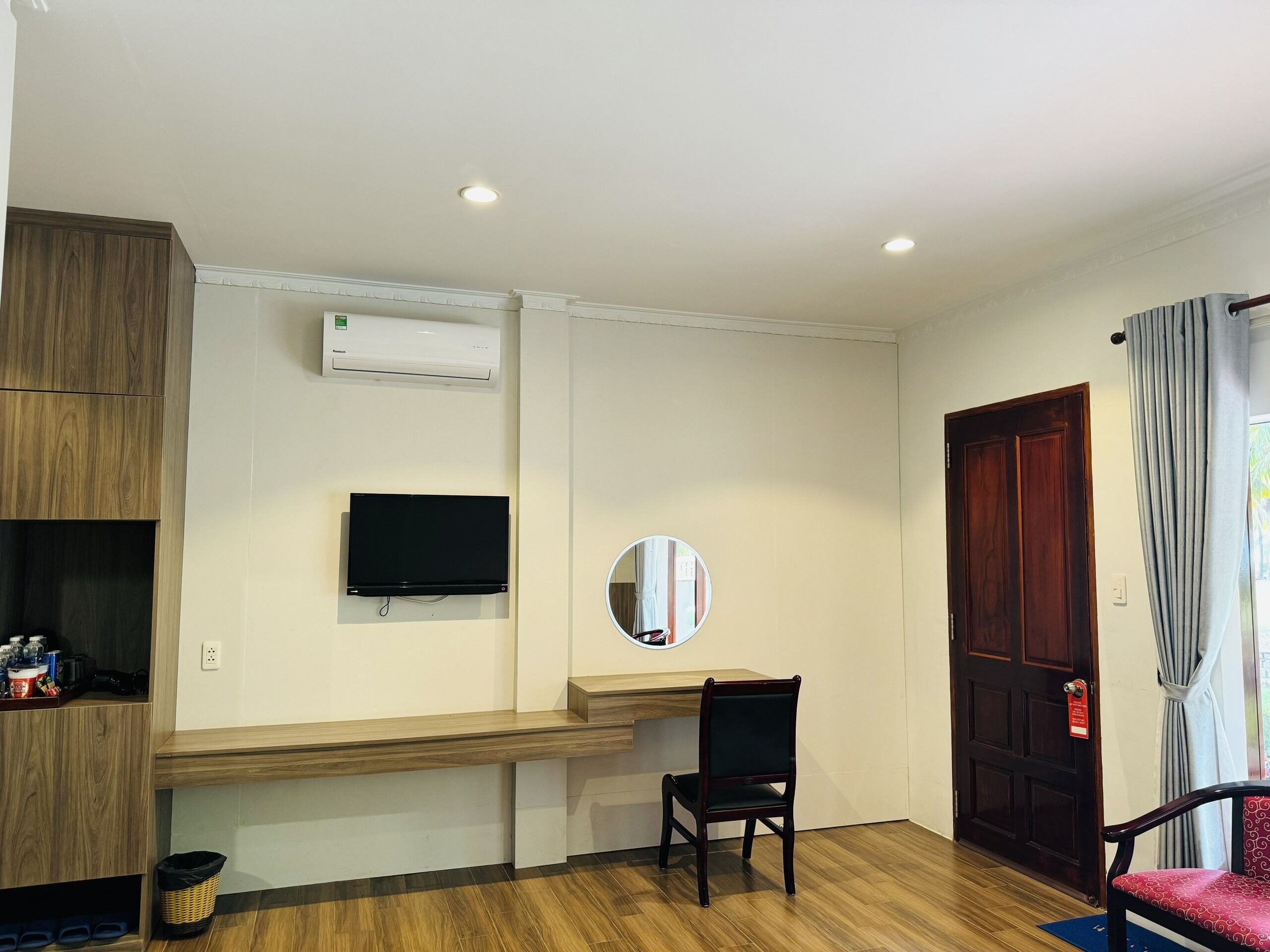 Une pièce avec un bureau en bois, une télévision, un miroir et une porte dotée d’une poignée rouge.