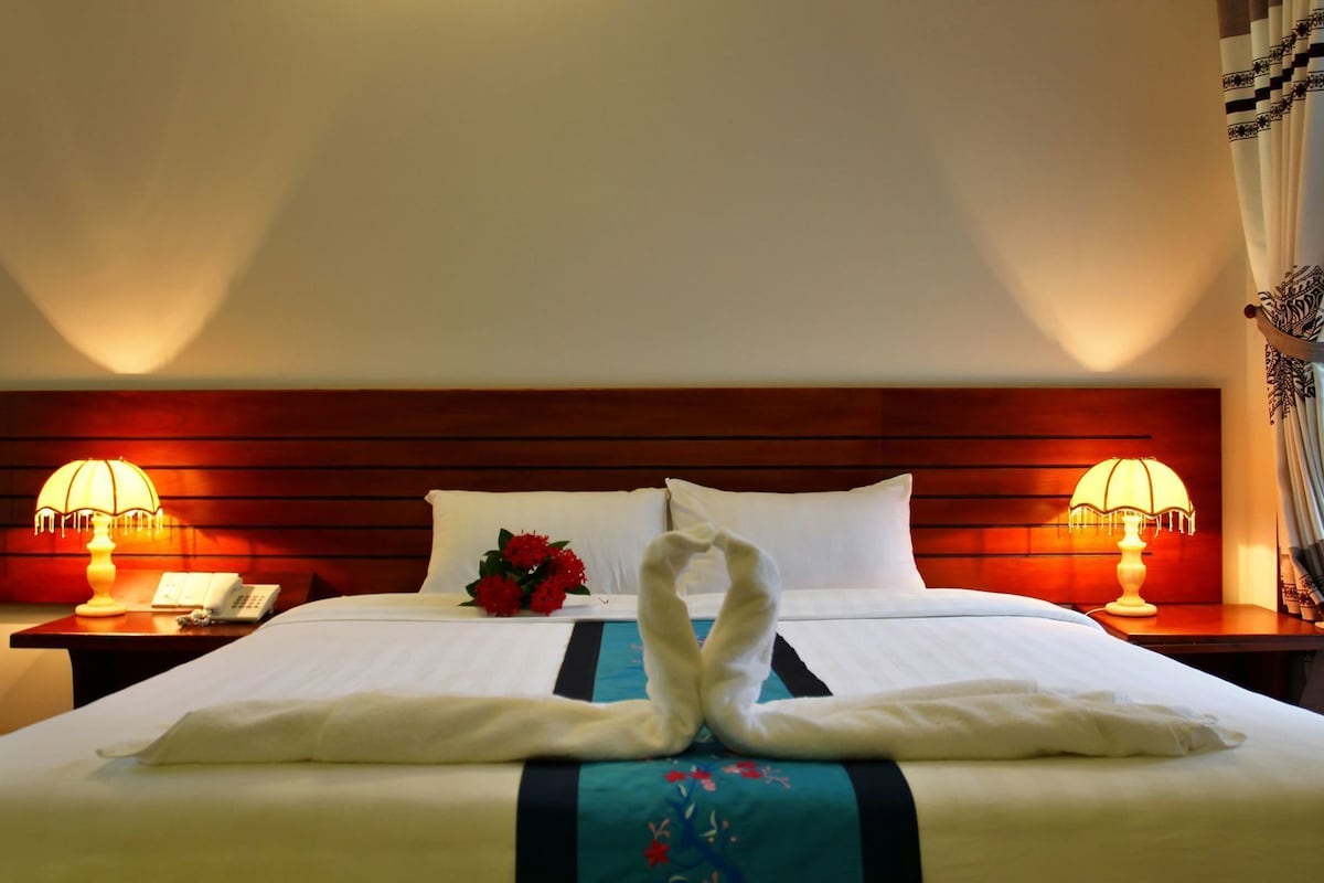 A hotel room with a neatly made bed, two bedside lamps, a telephone, and a floral arrangement.