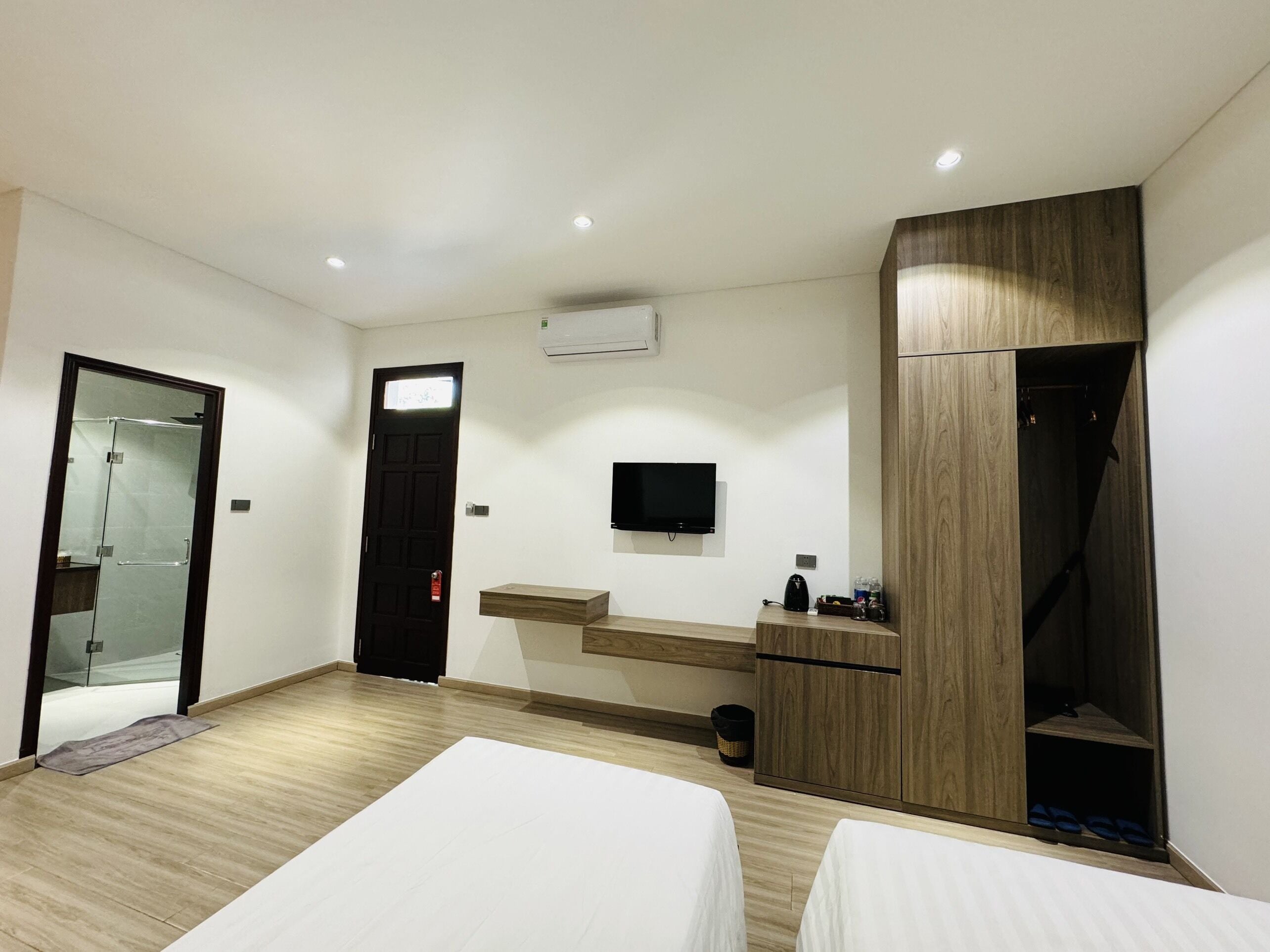 Una habitación de hotel moderna con dos camas, televisor, armario y zona de ducha.