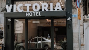 Het uiterlijk van Hotel Victoria met een duidelijke ingang, goed zichtbare borden en een geparkeerde auto.