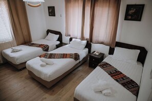 Une chambre d’hôtel avec trois lits simples, une table de chevet avec un téléphone et une fenêtre avec des rideaux.