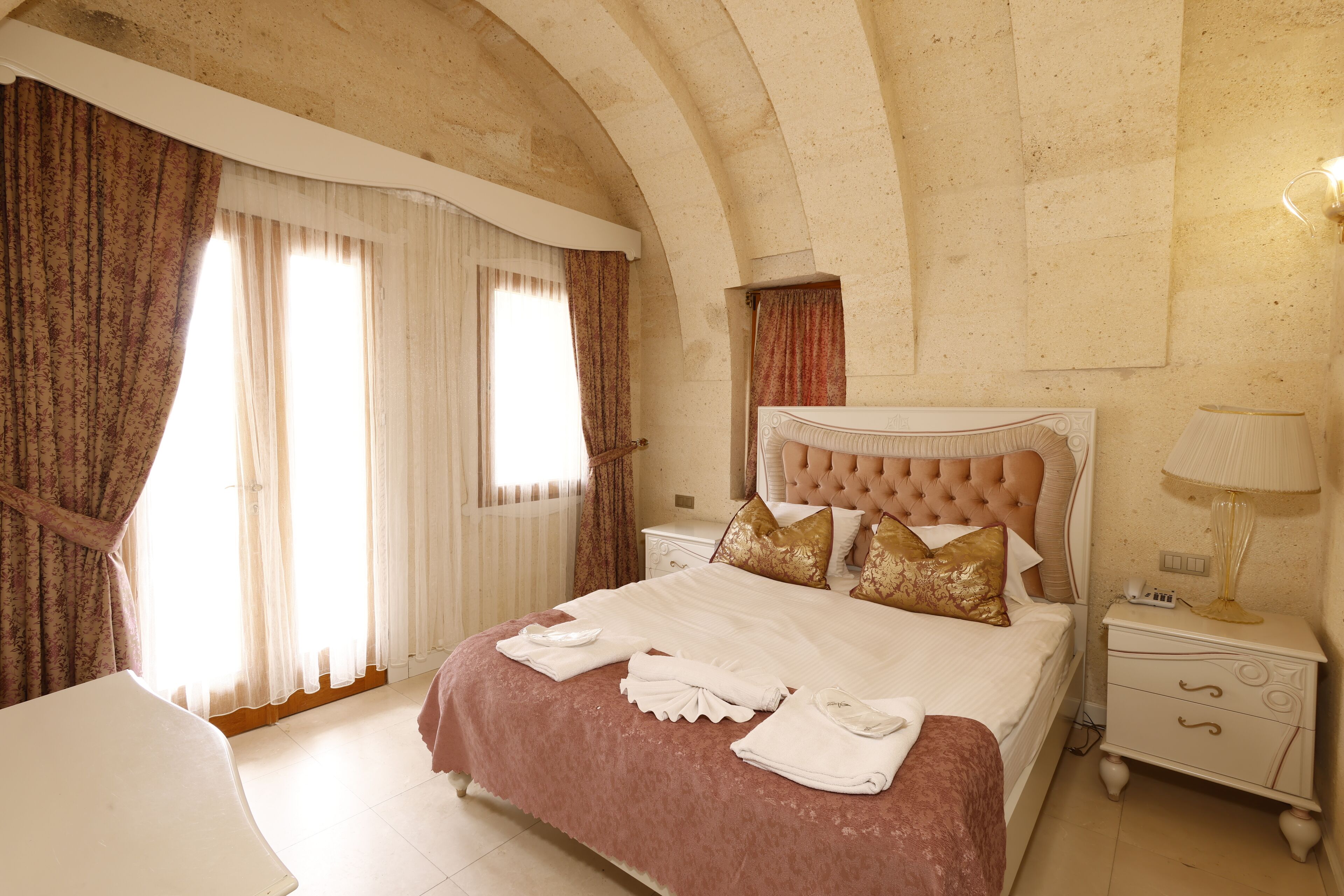 A hotel room with a large bed, a nightstand, a lamp, and curtains.