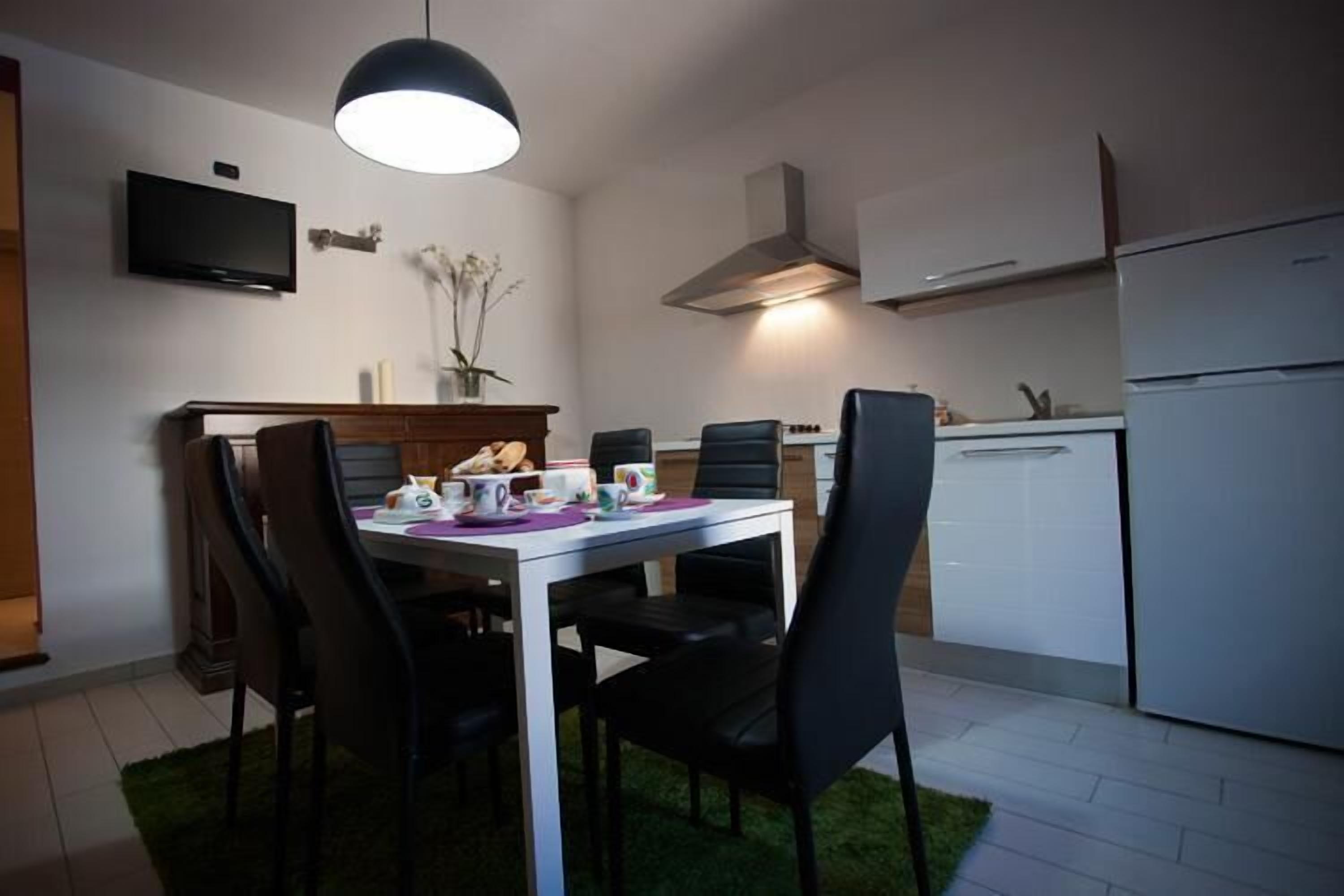 A modern kitchen with a dining area, white cabinets, a built-in oven, and a TV mounted on the wall.
