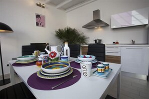 Une cuisine moderne avec des armoires blanches, une hotte de cuisinière en acier inoxydable et une table à manger agrémentée d’assiettes colorées et d’un vase.