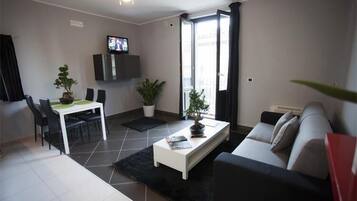 Un salon moderne comprenant un canapé, une table basse et un coin repas avec des chaises et un téléviseur.