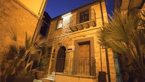 Een gebouw van steen met een balkon en een toegangspartij met bogen, omgeven door potplanten.