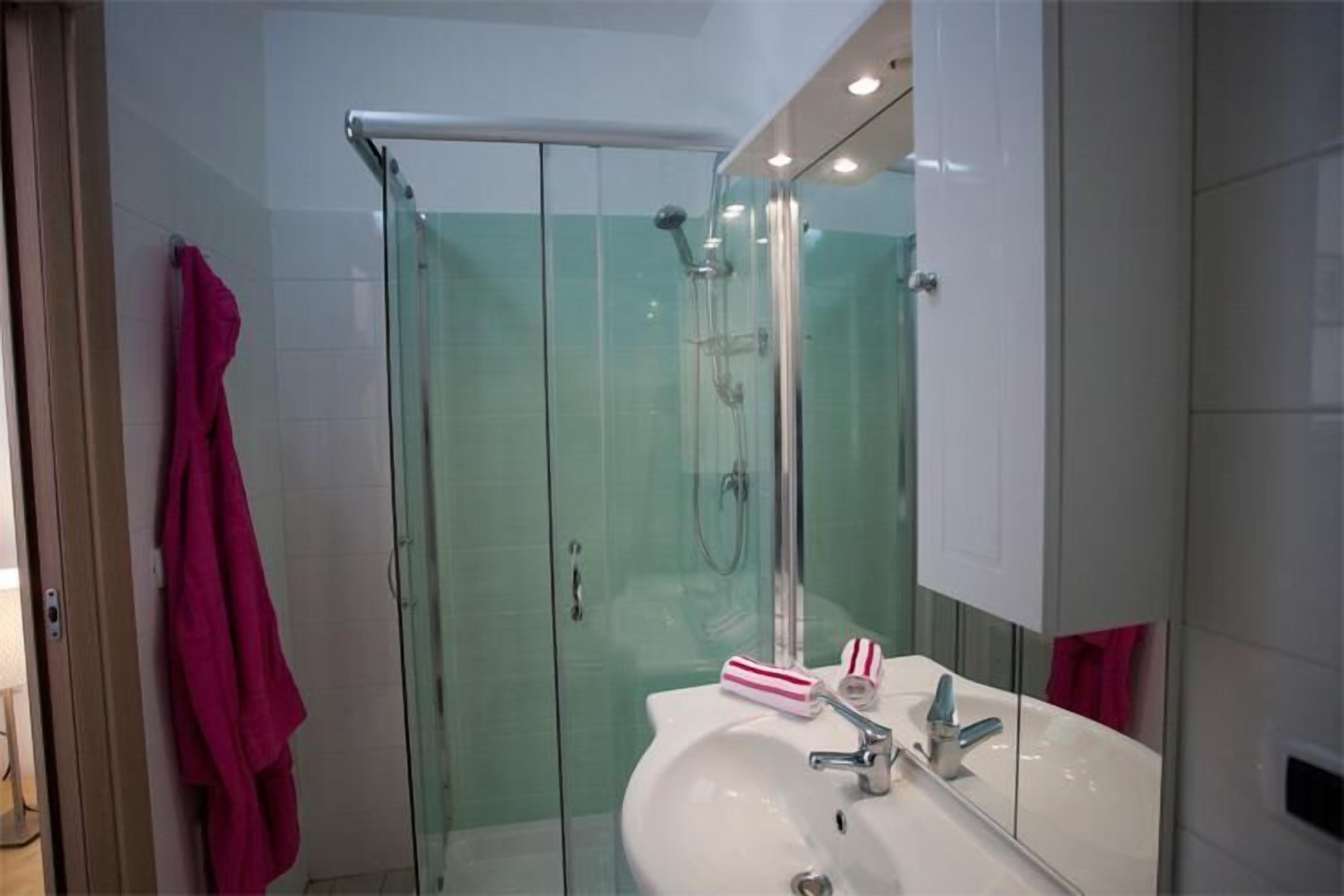 Ein modernes Badezimmer mit einer gläsernen Duschkabine, einem weißen Waschbecken und einem Spiegel.