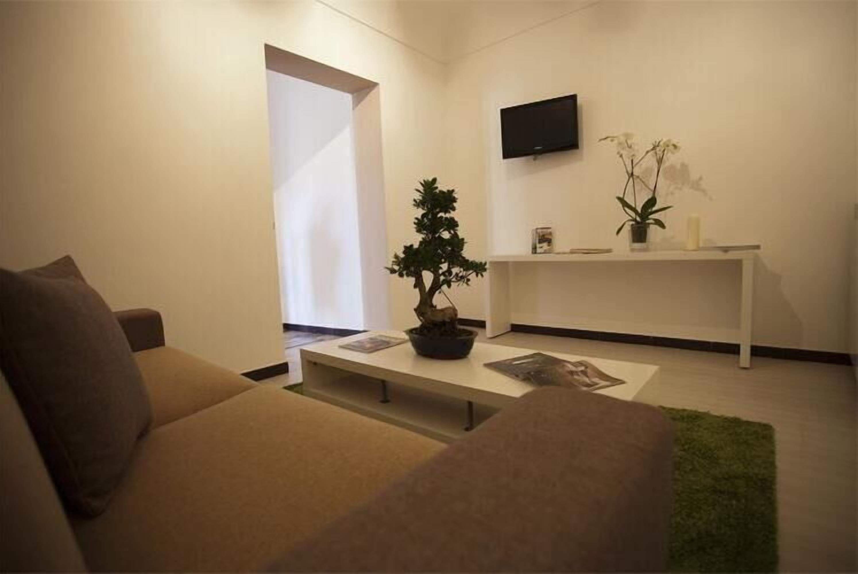 Un soggiorno moderno con un divano, un tavolino da caffè con un bonsai, una TV a schermo piatto montata a parete e una piccola mensola con oggetti decorativi.