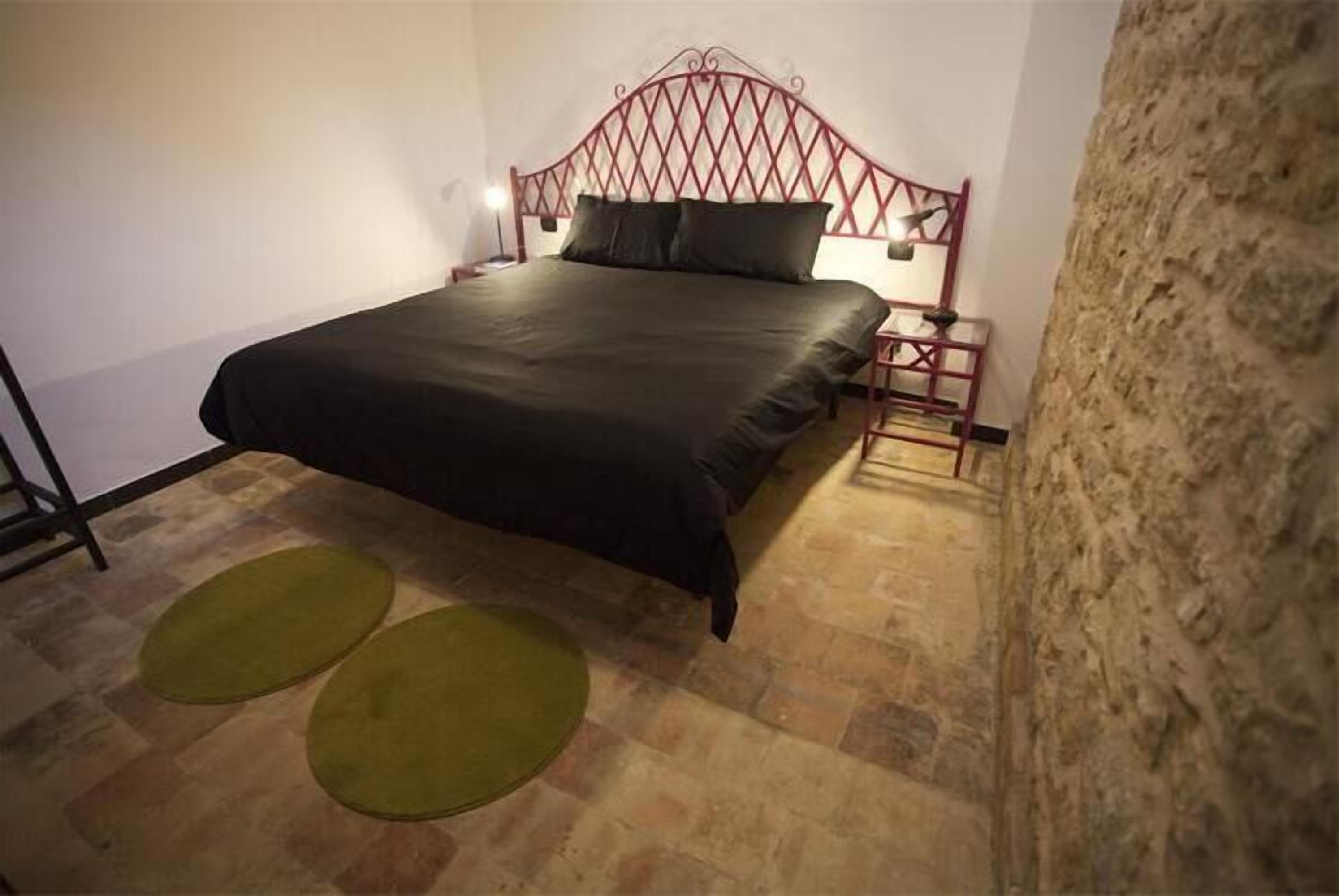 A bedroom with a bed, a nightstand, a lamp, and two green rugs.