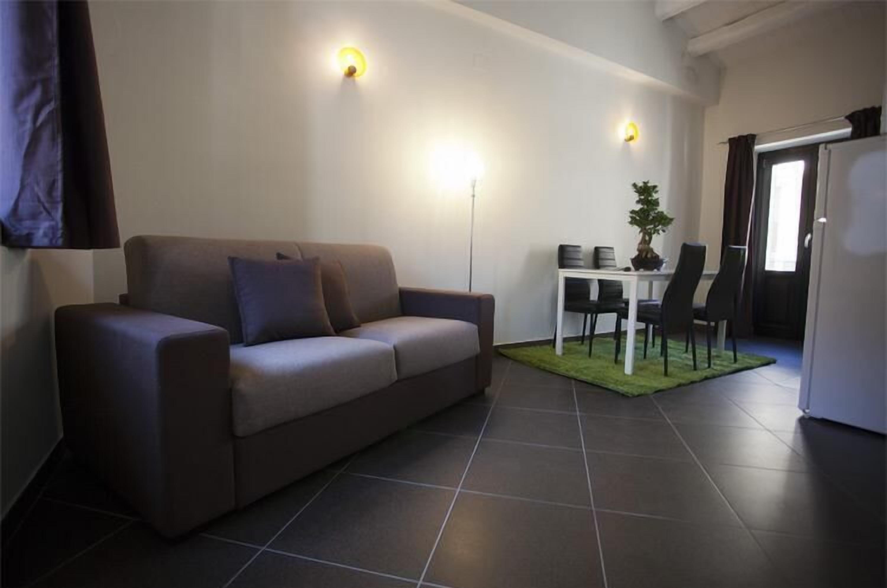 A modern living room with a sofa, a dining table with chairs, and a small kitchen area.