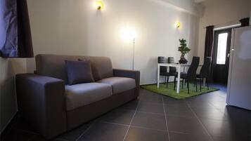 A modern living room with a sofa, a dining table with chairs, and a small kitchen area.