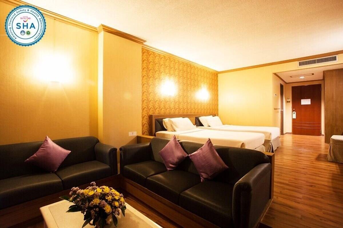 A hotel room with two black leather sofas, a bed with white linens, and a wooden floor.