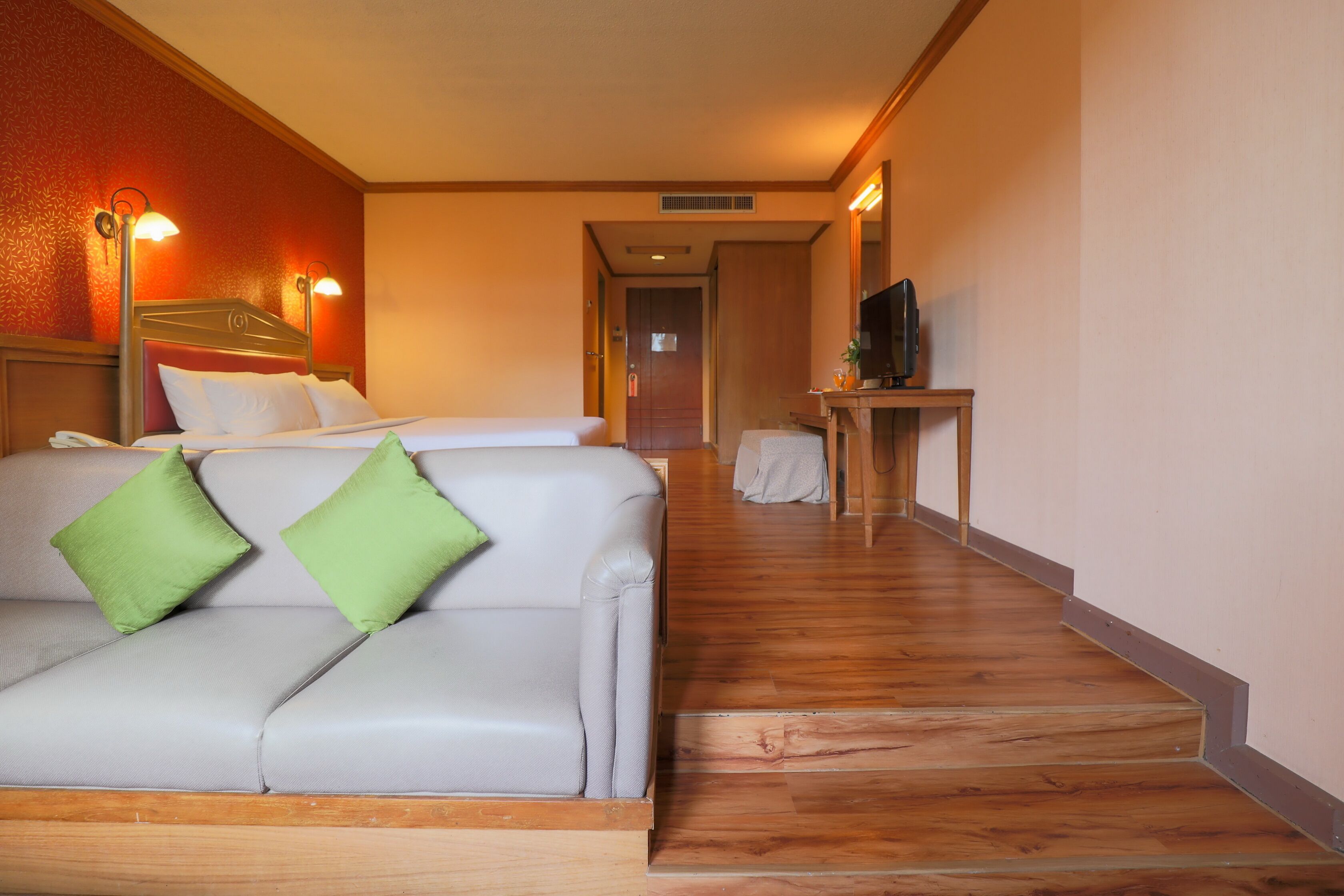 A hotel room with a bed, a sofa with green cushions, a wooden floor, and a television on a small table.