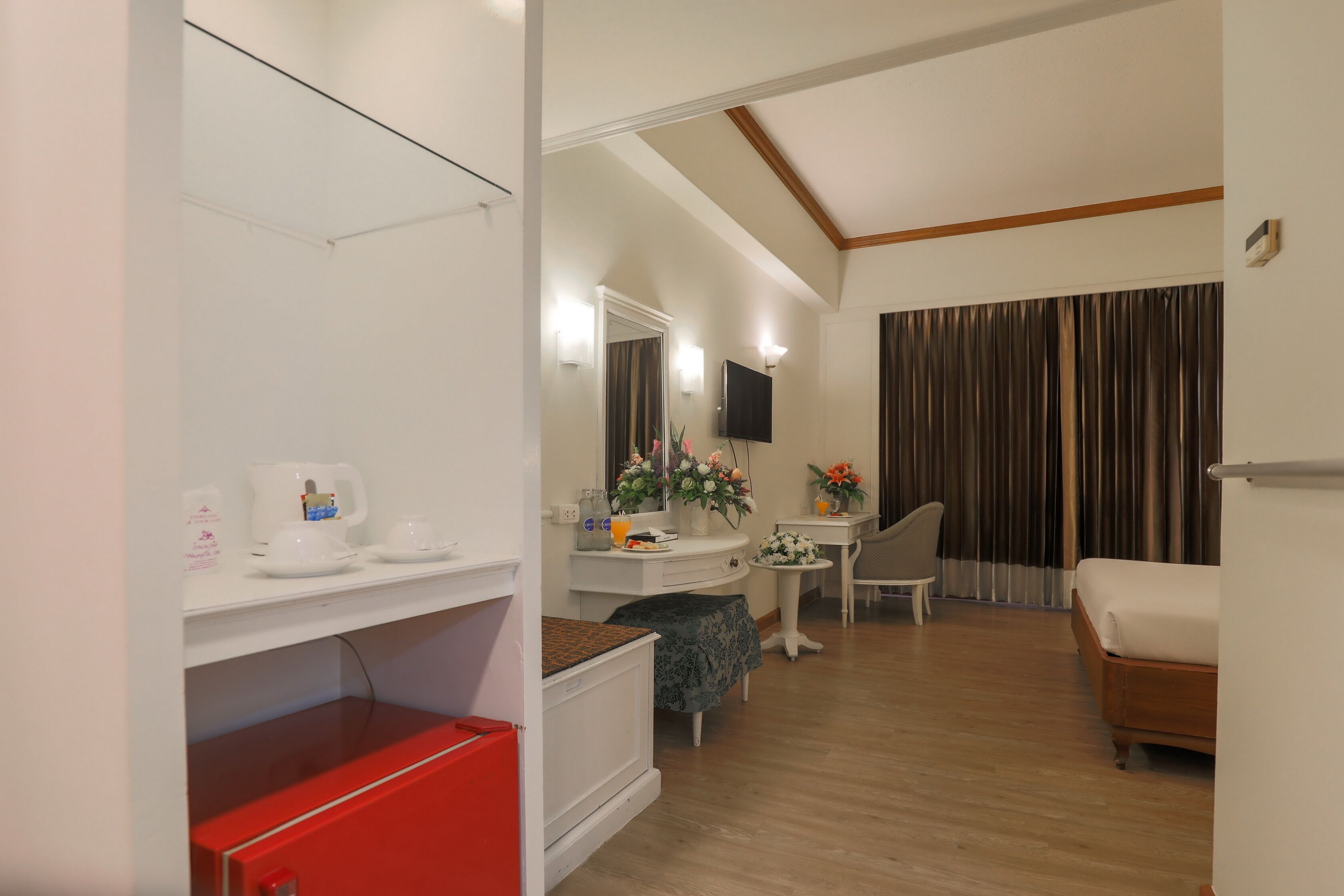 Una habitación de hotel con una cama, un escritorio, una silla, una mesita con un jarrón de flores y un espejo sobre otro espejo.