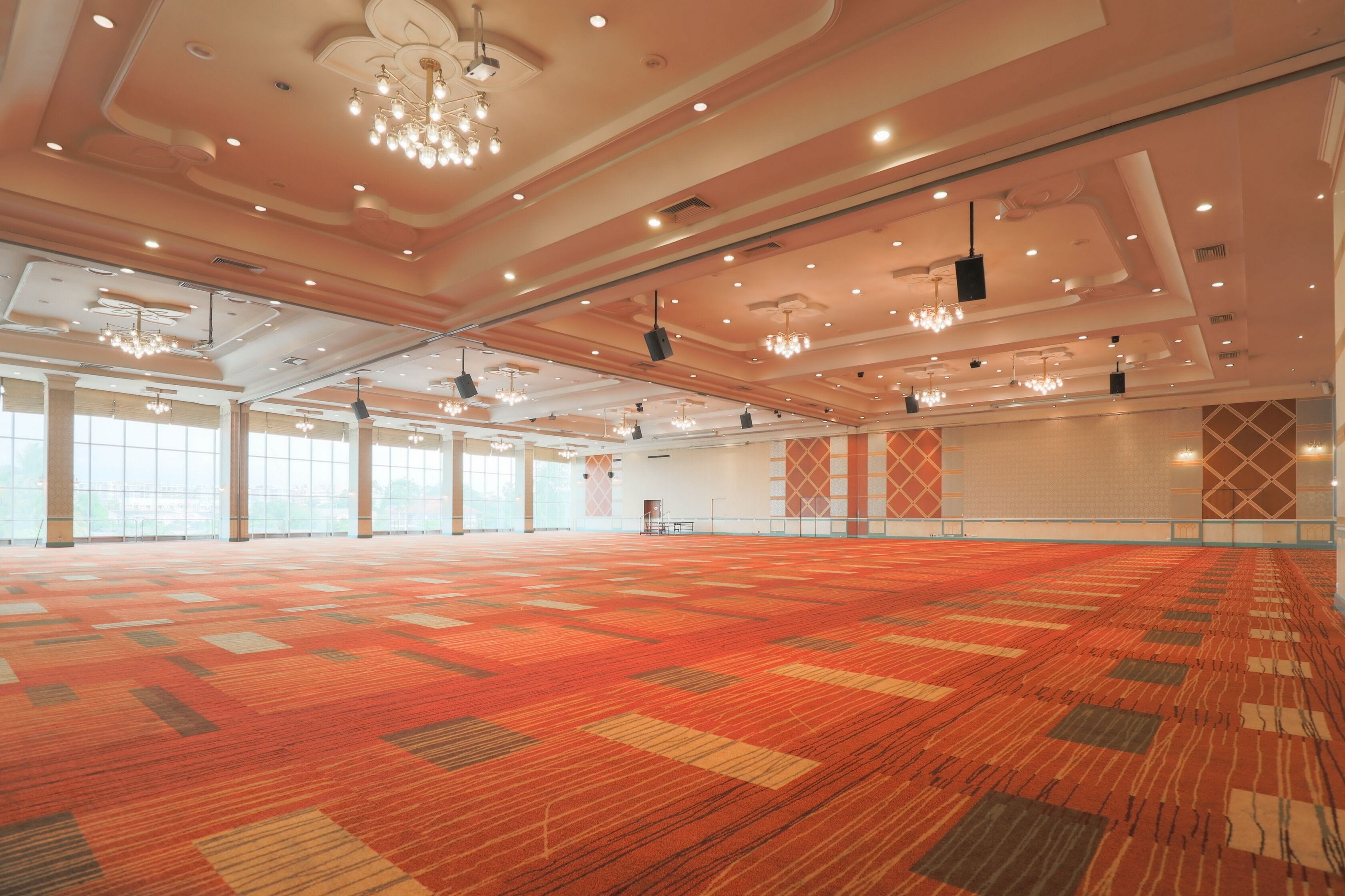 Ein geräumiger Saal mit Teppichmuster, großen Fenstern und modernen Kronleuchtern.