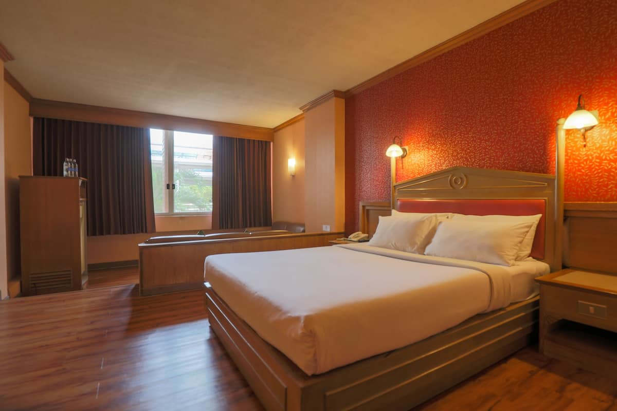 A hotel room with a large bed, a desk, a chair, and a wardrobe.
