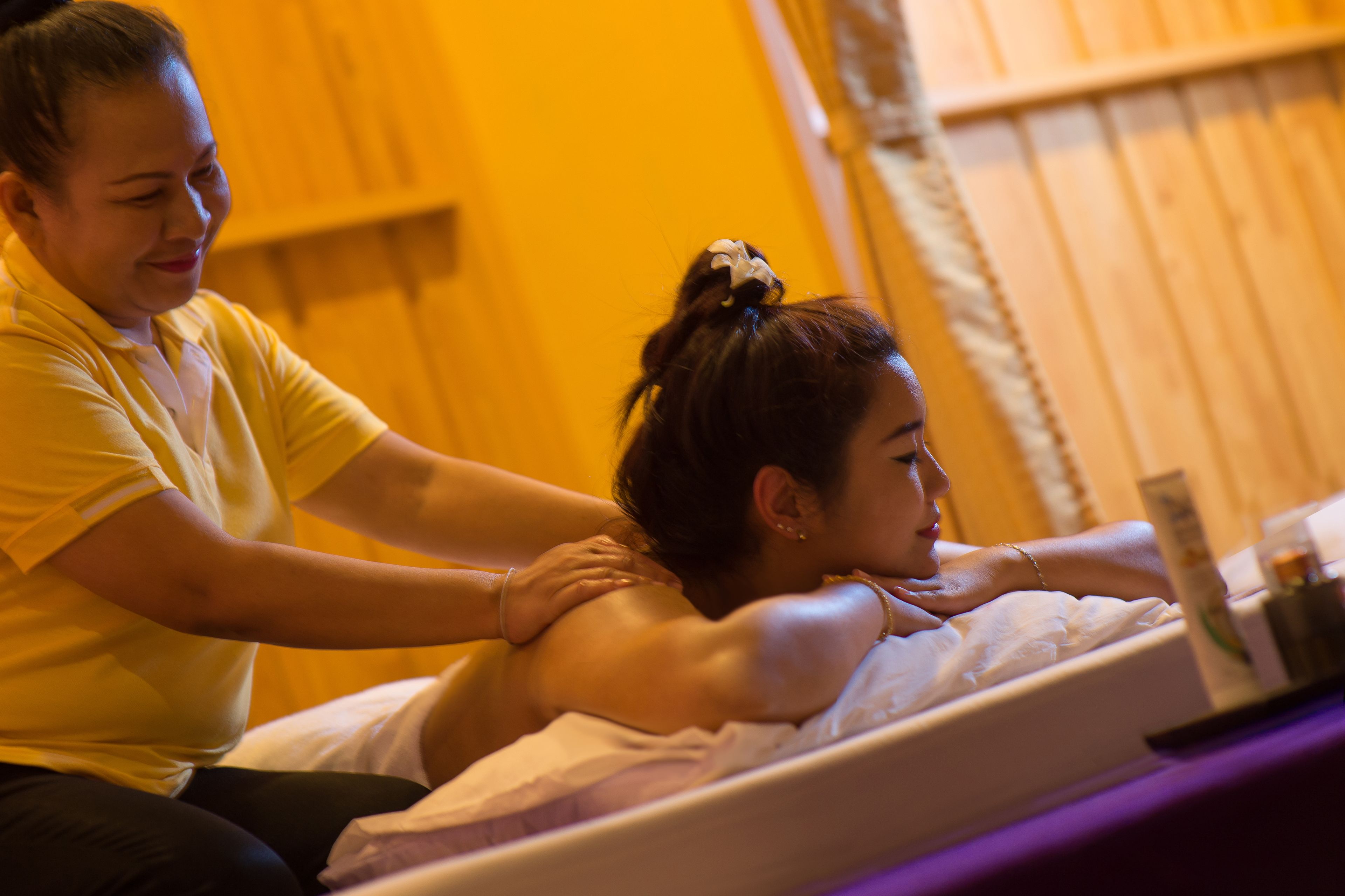 A person receiving a massage in a room with wooden walls and a bed with a white mattress.