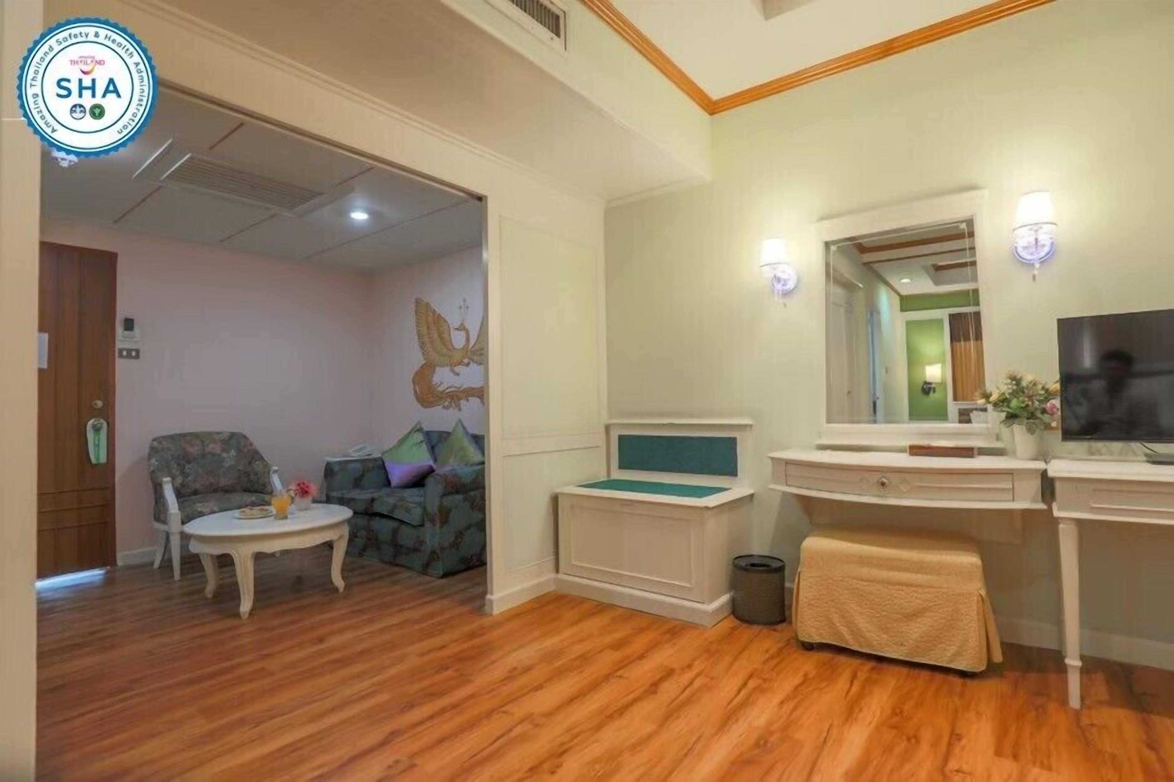 A hotel room with a wooden floor, a sofa, a small table, a desk, and a television.