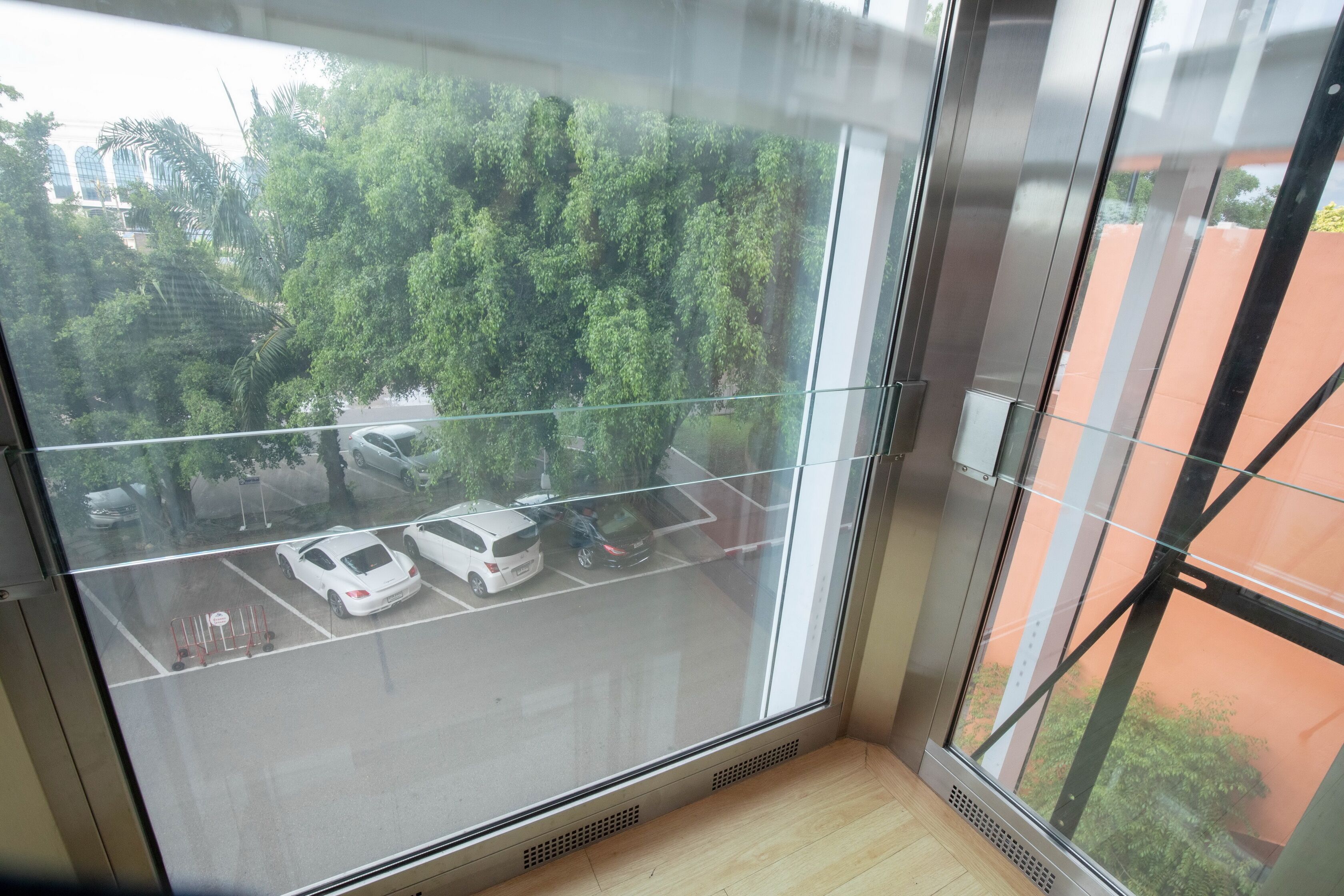 A view from a window in a building, looking out at a parking lot with several cars and trees.