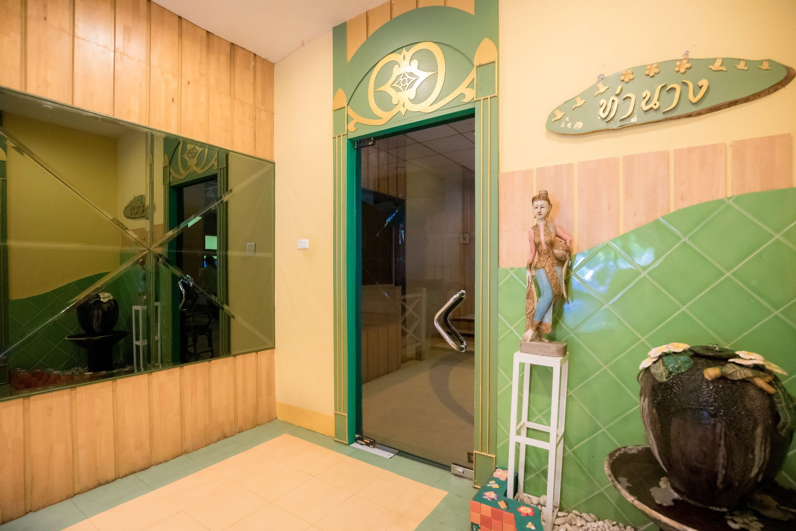 A bathroom with a green and beige color scheme, a large mirror, a decorative statue, and a tiled wall.