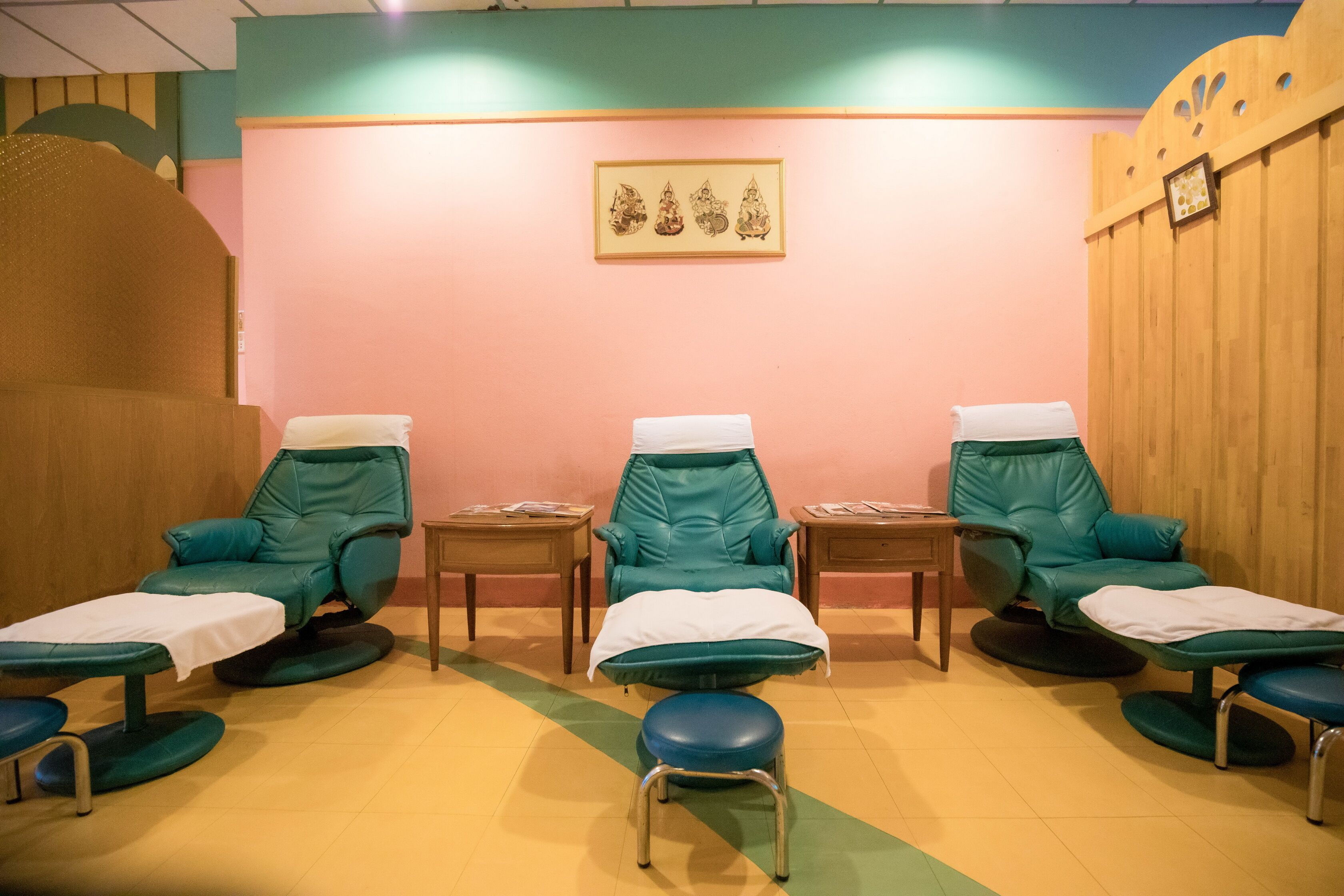 A room with four green massage chairs, each with a footrest and a small table.