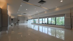 A spacious, modern hotel lobby with a polished floor, large windows offering a view of greenery and buildings, and a neutral color palette. - Wangtai Hotel (Surat Thani)