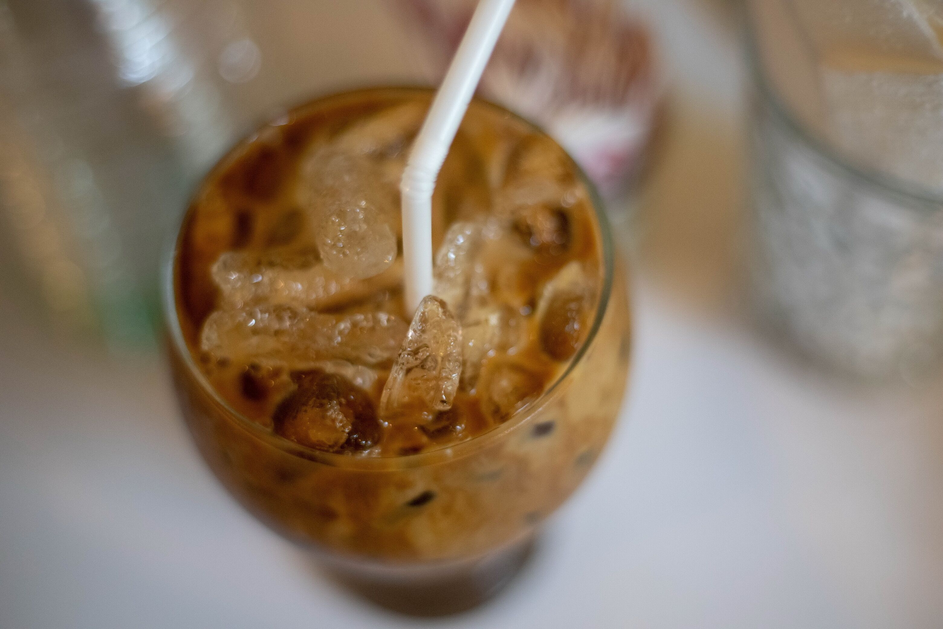 A close-up of a glass with a straw, containing a beverage with ice cubes.