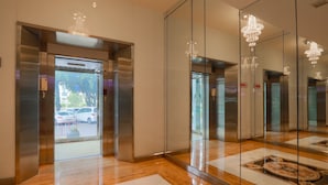 A modern elevator area with glass doors, a stainless steel elevator, and a chandelier. - Wangtai Hotel (Surat Thani)