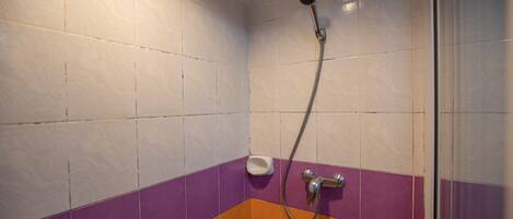 Une salle de bain avec des murs carrelés de blanc et de violet, une douche avec un pommeau de douche amovible et un distributeur de savon.