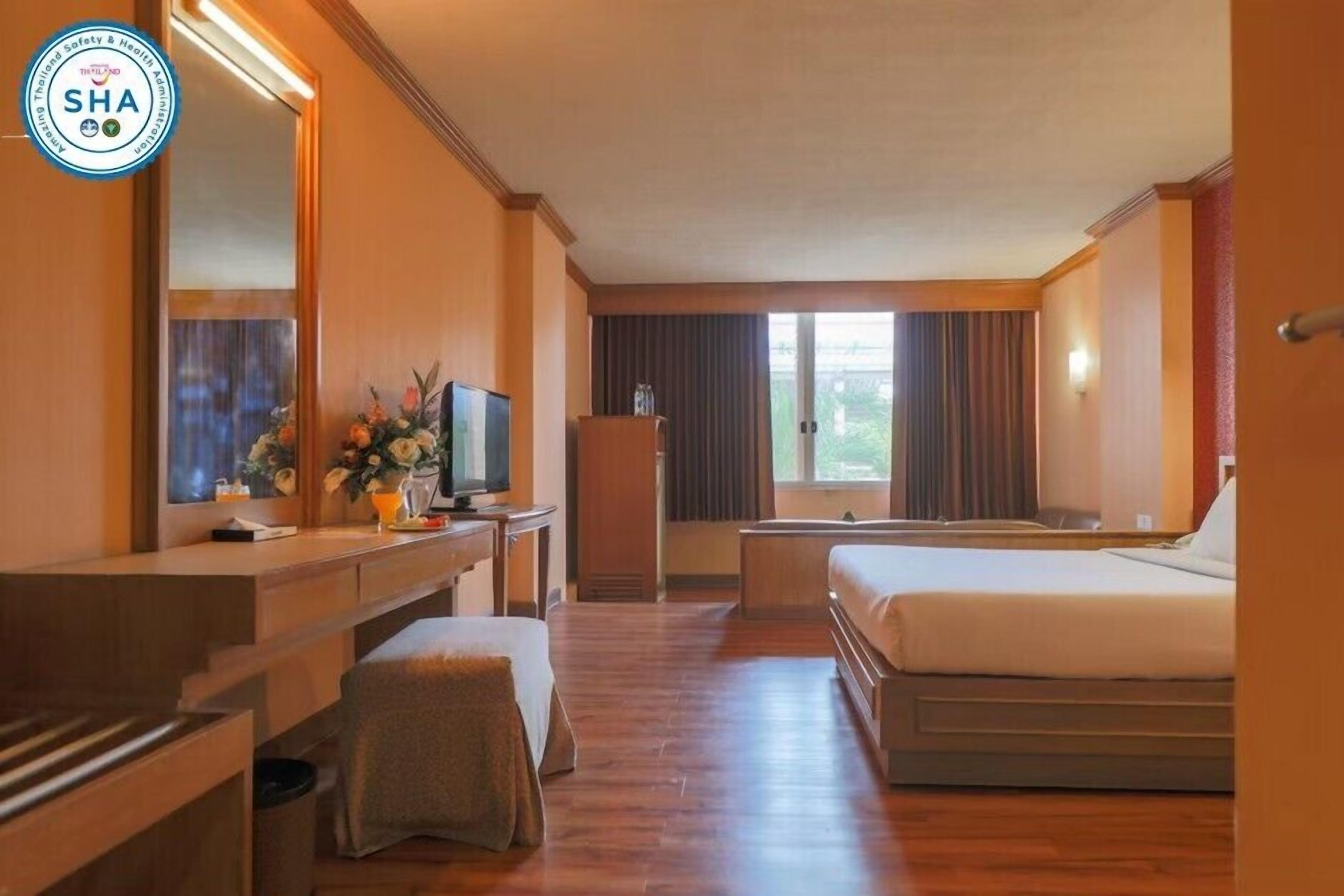A hotel room with a wooden floor, a desk with a television, a bed, and a window with curtains.