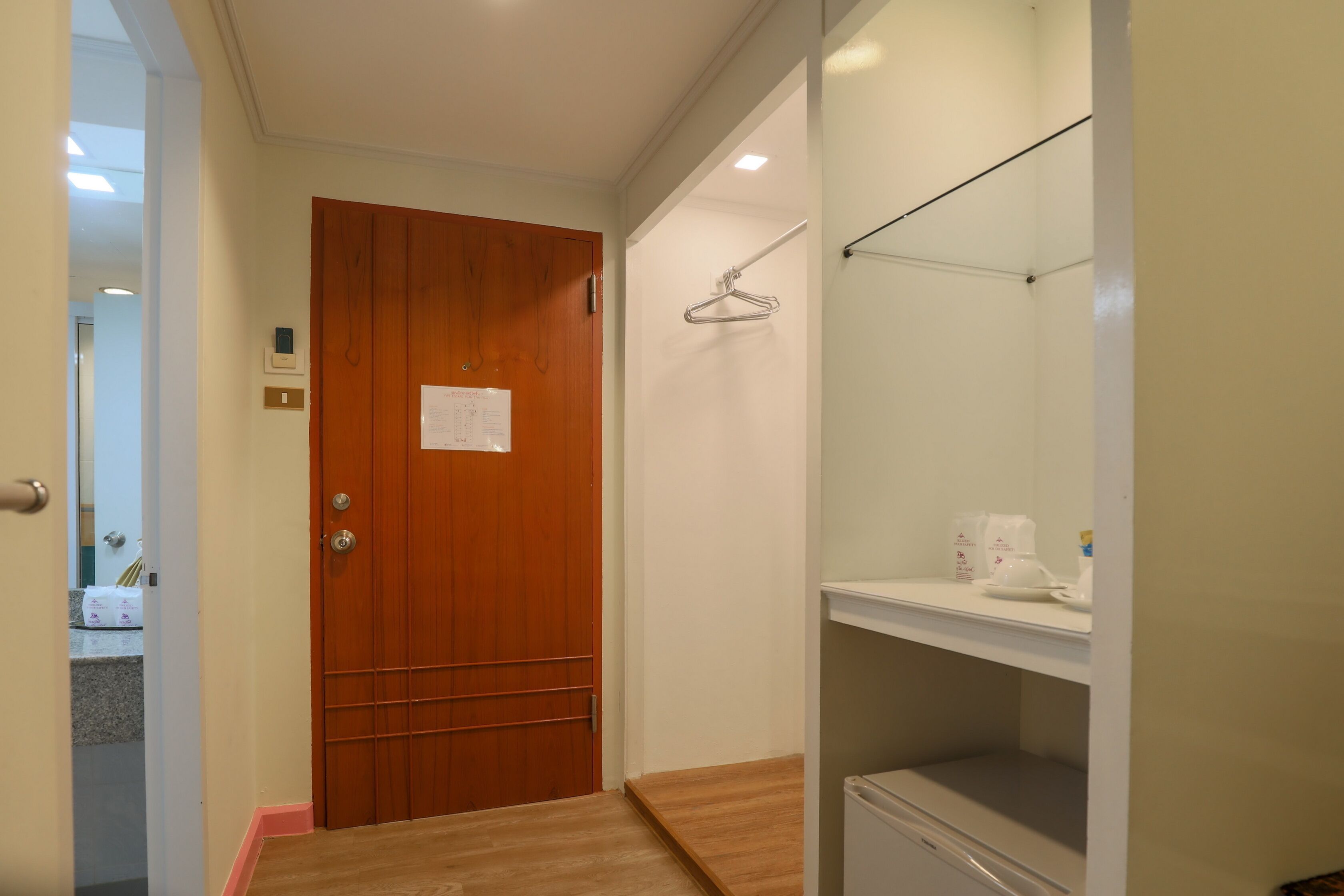 A hallway with a wooden door, a coat rack, and a white shelf with a coffee maker.