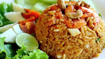 Plato de arroz frito cubierto de camarones, anacardos y vegetales, acompañado de una ensalada.
