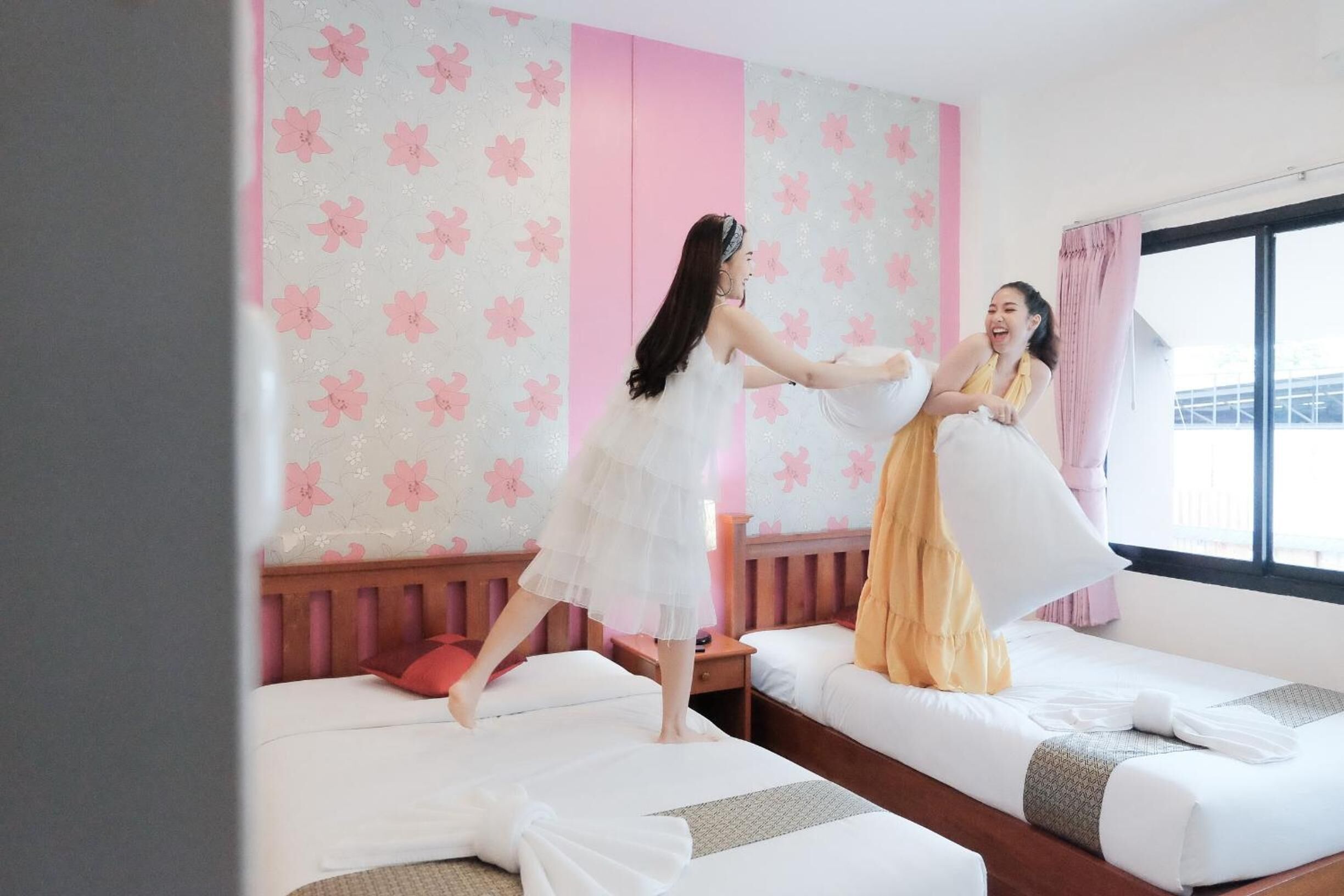 A hotel room with two beds, a pink and white floral wallpaper, and a large window with a view.