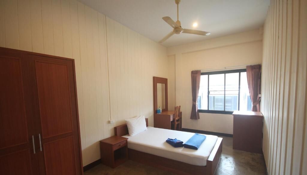 A bedroom with a bed, a desk, a chair, a wardrobe, and a window with curtains.