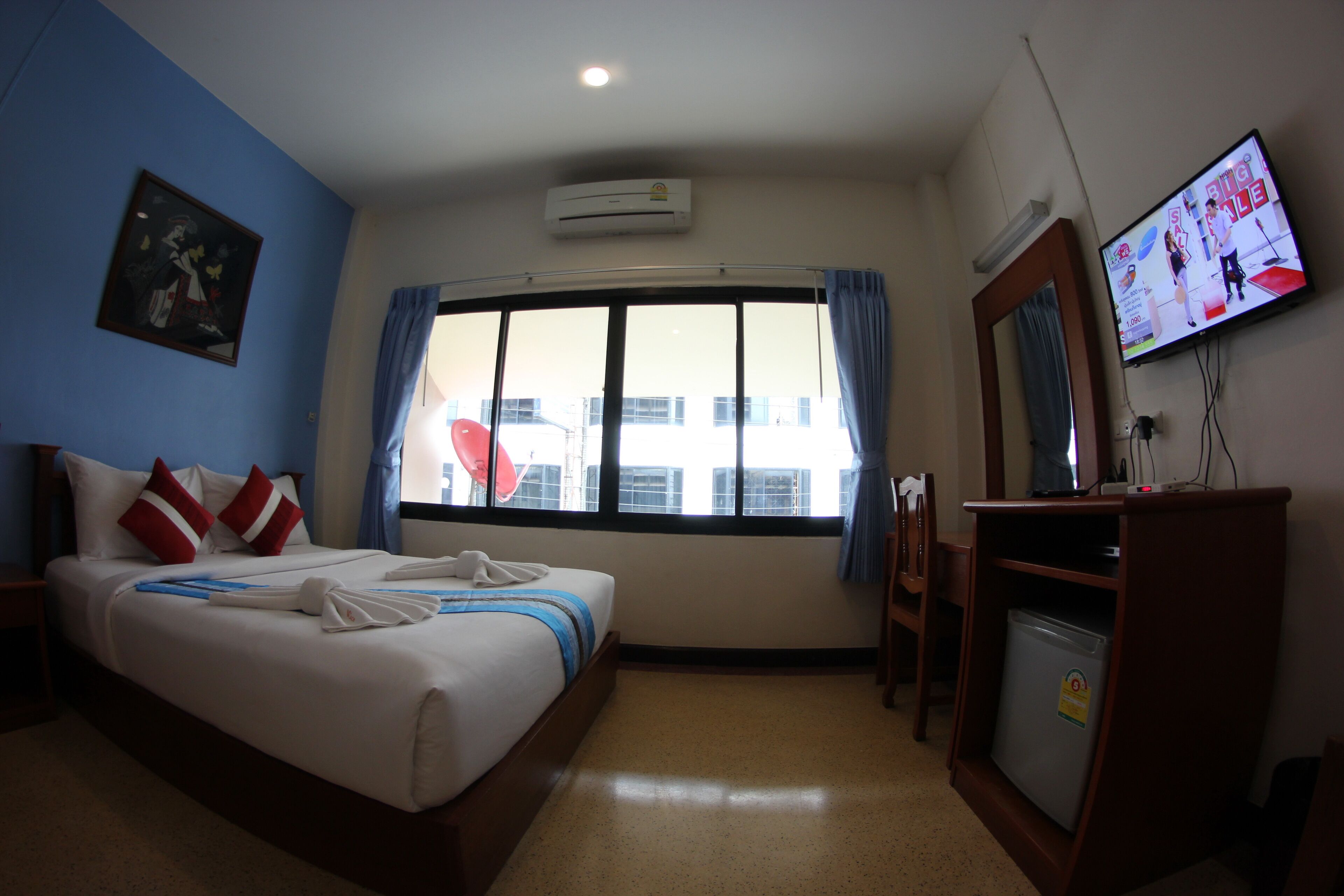 Una habitación de hotel con cama, televisor, escritorio y ventana con cortinas.