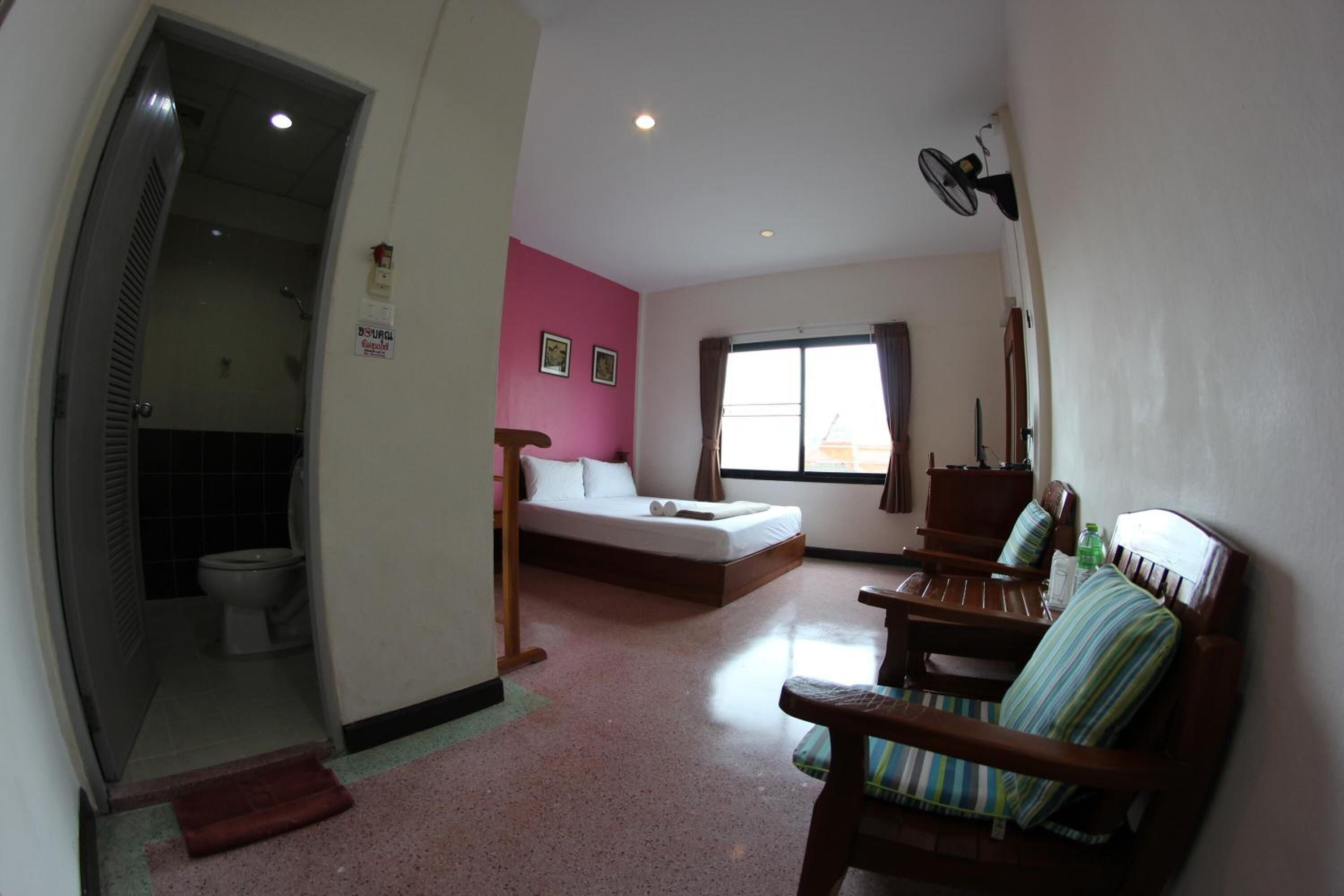 Um quarto com cama, uma cadeira, uma janela e porta de acesso a um banheiro.