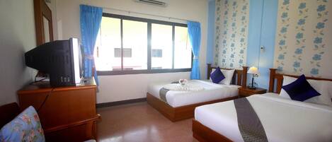 A hotel room with two beds, a television on a wooden dresser, a chair with floral upholstery, and a window with blue curtains.